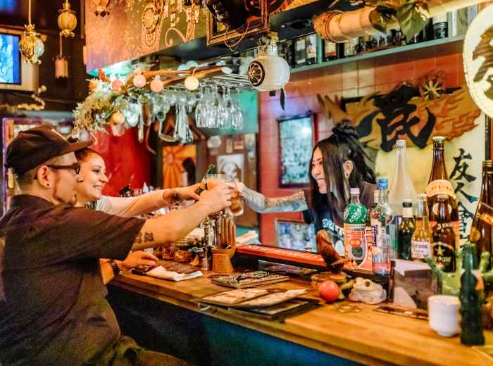 Guests clinking drinks at an izakaya with host smiling.