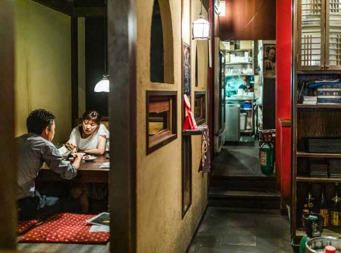 A cozy, traditional izakaya tucked into a narrow alley, with warm light spilling from its entrance and traditional lanterns creating an intimate atmosphere.