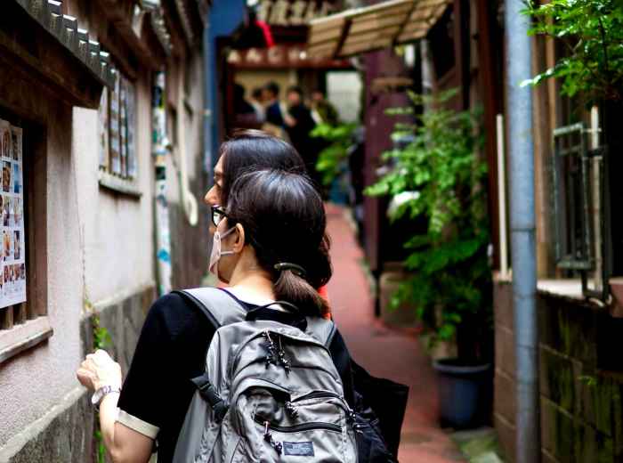 A confident solo traveler walking alongside a friendly local host through a traditional neighborhood, both engaged in animated conversation. Image by Kazuo Ota on Unsplash.