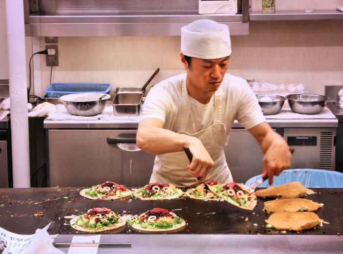 Chef preparing okonomiyaki on a large griddle 