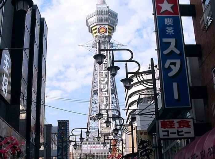 Street-level view of Tsutenkaku Tower showing its distinctive steel structure against the urban backdrop. Image by Stephen Harlan on Creative Commons Attribution 2.0