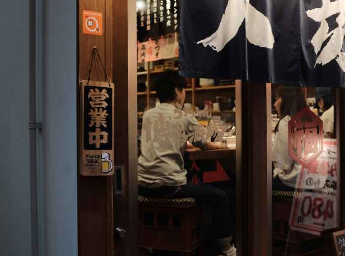 A regular customer shares a friendly conversation with the restaurant owner inside a cozy Shinsekai eatery. Images by Mak on Unsplash.