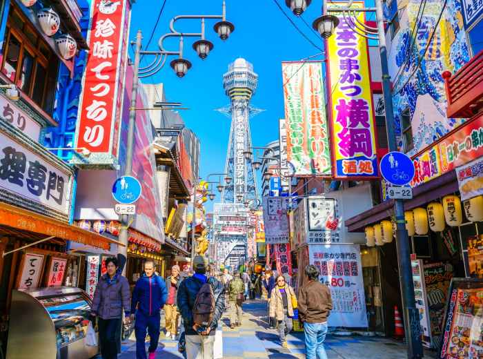 Shinsekai street at dusk with glowing signs and a soft, warm light marking the end of the day.