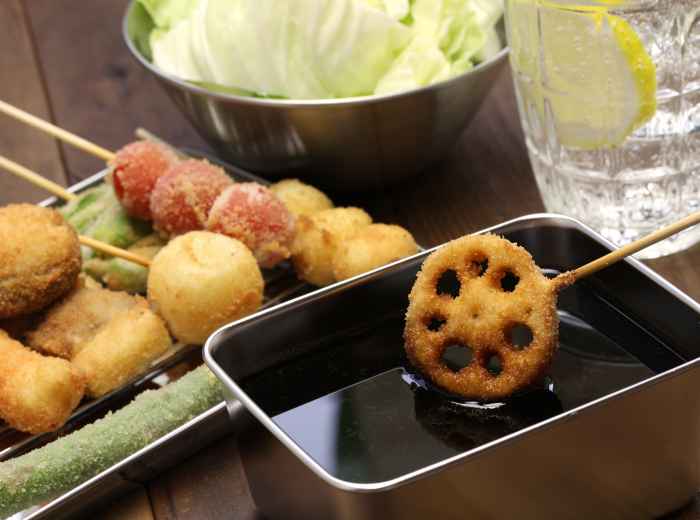 Kushikatsu skewers being dipped in sauce at a street stall.