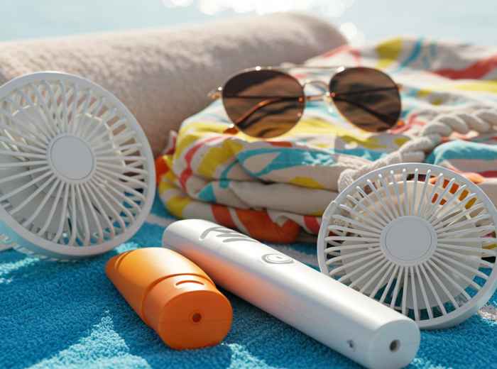 Summer essentials laid out including fan, sunscreen, and towel