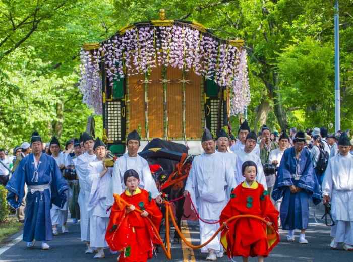 People in Heian period costumes walk in the Aoi Matsuri festival procession surrounded by Kyoto’s springtime scenery.