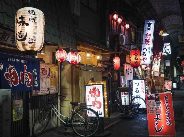 A bustling nighttime scene with street food stalls and locals gathering for dinner and drinks.