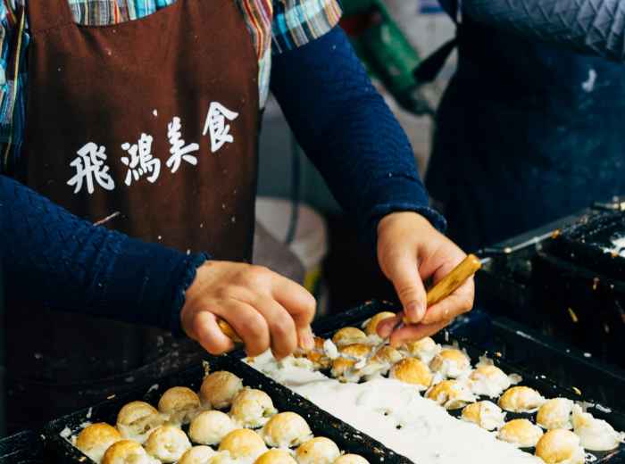 Takoyaki sizzling on a pan with chef's hands working the tools Photo by Markus Winkler on pexels