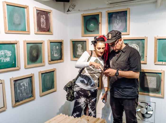 Close-up shot of a traveler and host having an intimate conversation while examining intricate details of a traditional craft at a small artisan workshop