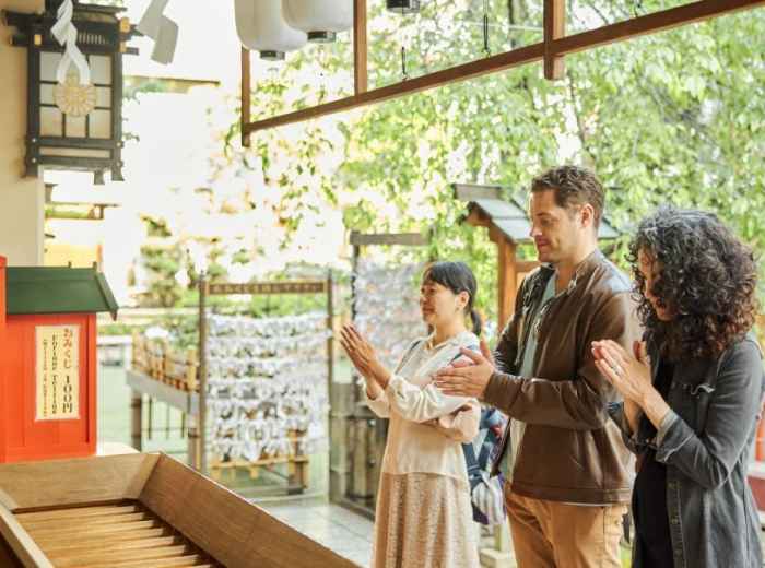 Host demonstrating proper etiquette at a traditional shrine while travelers observe respectfully.