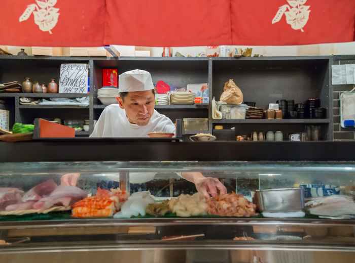 A guide talking with guests about seasonal foods at a fresh market stall.