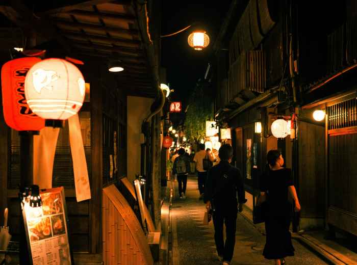 A small group walking through a quiet alley with traditional wooden buildings and lanterns.Photo by ayumi kubo on Unsplash