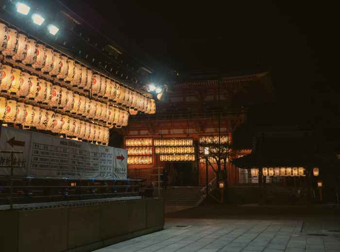 Night view of traditional Kyoto district with illuminated temple lanterns and wooden buildings contrasting against distant city lights Photo by Andy Li on Unsplash