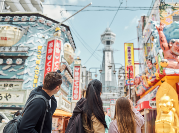 Tsutenkaku Tower rising above the bustling streets of Shinsekai district with local shops and restaurants below.