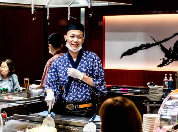 Smiling host explaining dish history to engaged guest while holding traditional cooking utensil. Photo by hiurich granja on Unsplash