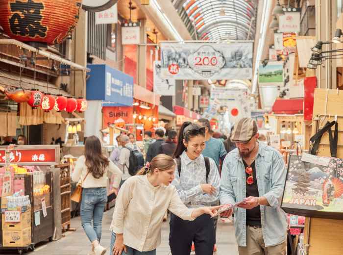 Narrow walking path through Kuromon Market with vendors on both sides and natural lighting.