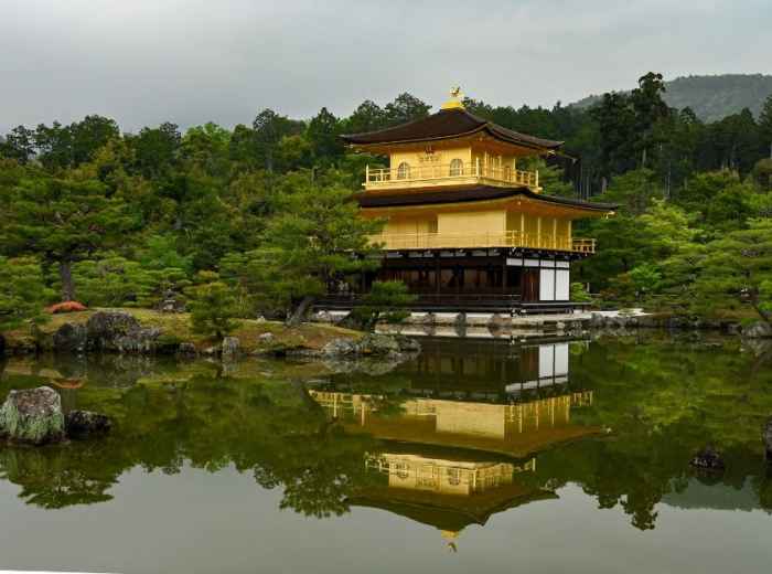 Morning mist rising from pond surrounding Kinkaku-ji Temple with golden pavilion reflected in still water.