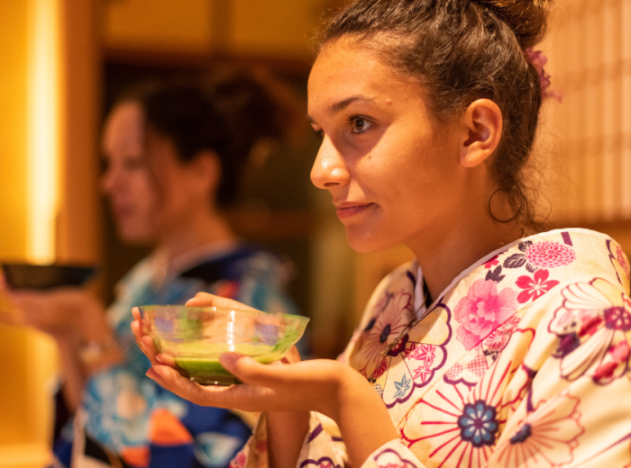 A traveler participating in a traditional tea ceremony, with a tea master demonstrating precise movements in a serene Kyoto setting