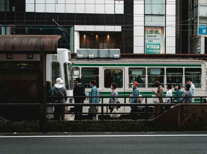 Passengers boarding a bus at a busy Kyoto intersection with traditional and modern buildings visible Photo by Christian Chen on Unsplash