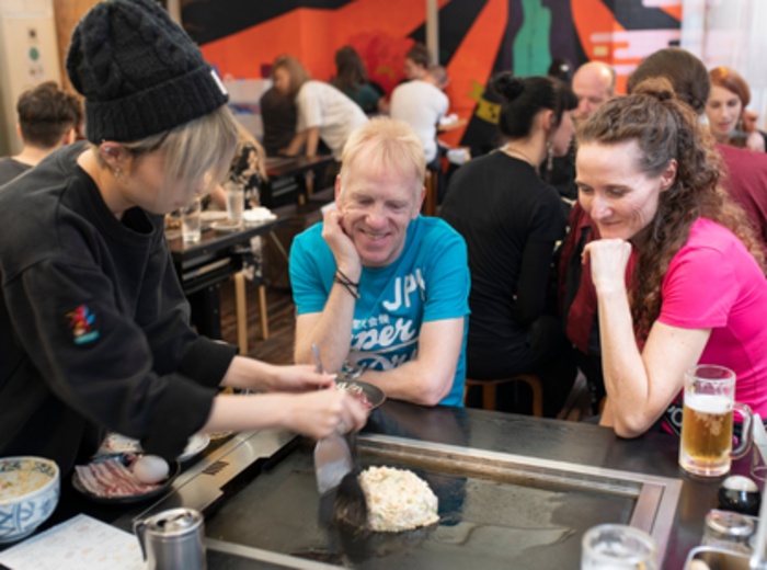 Local okonomiyaki restaurant with chef cooking on traditional griddle.