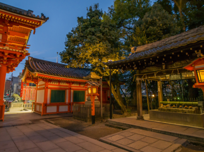 Warm lantern light illuminating stone lanterns and a vivid orange torii gate in the quiet of evening