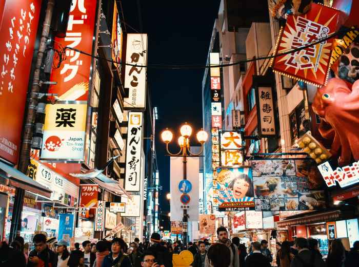 Crowds explore brightly lit streets lined with colorful neon signs in Osaka’s bustling entertainment district