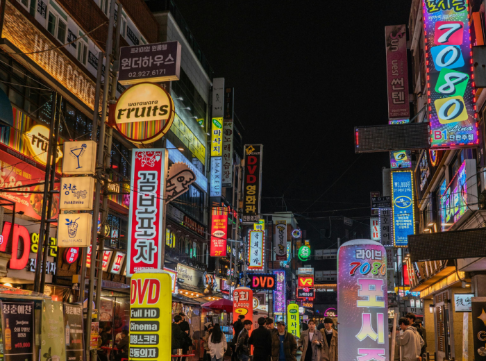 Street scene in Hongdae with neon signs and young people walking 