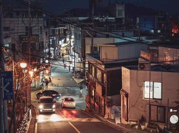 A quiet Seoul street at night with well-lit pathways and car slowly passing through the city