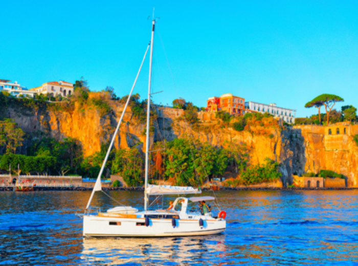Small sailboat on calm sea beside sunlit coastal cliffs