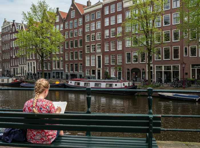 Local resident sketching canals from bench, typical Amsterdam scene