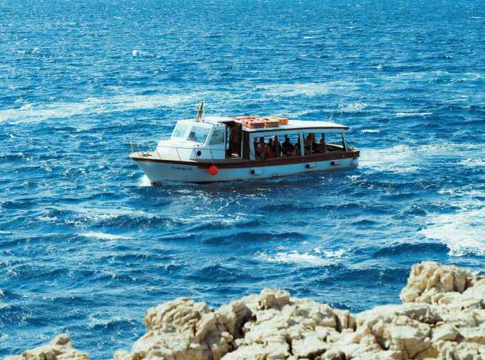 Small ferry boat on blue Mediterranean waters near rocky coast