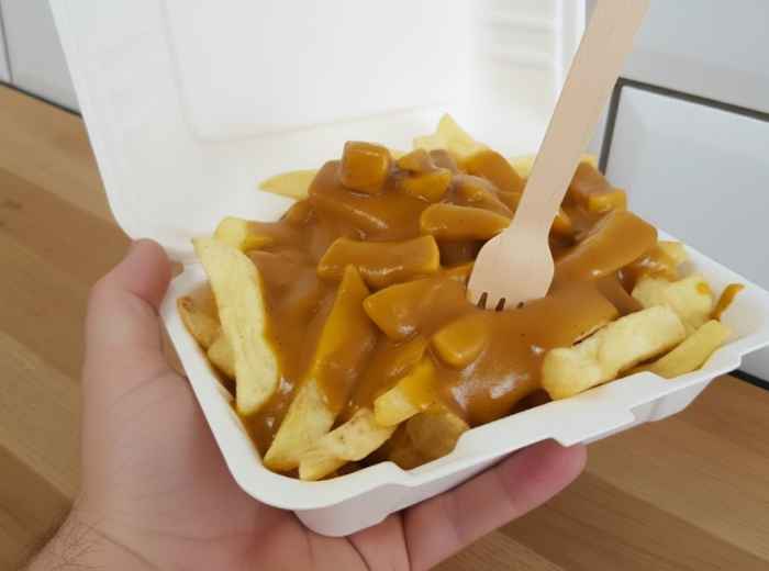 Takeaway curry chips in a cardboard tray with wooden fork