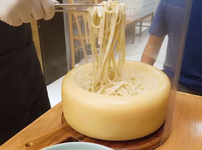 Chef tossing cacio e pepe in hollowed pecorino wheel at tableside