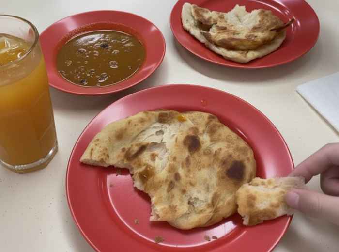 Golden roti prata torn open showing flaky layers with curry dipping sauce
