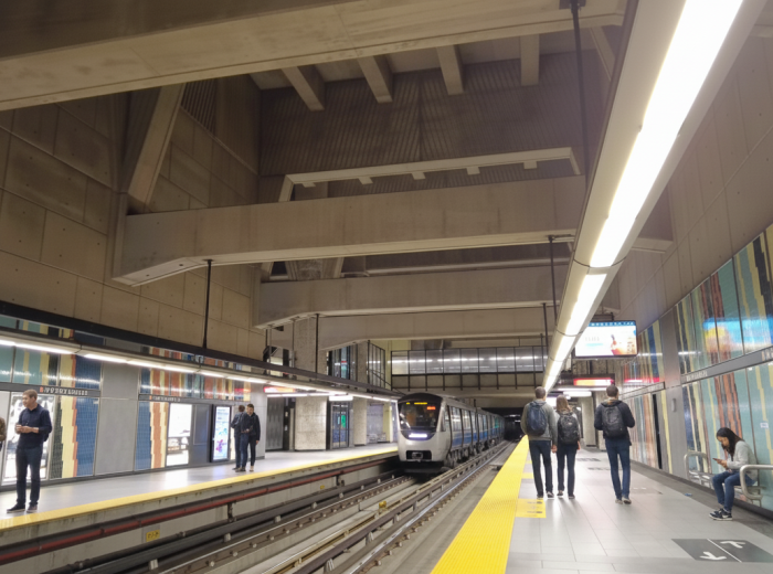 Orange line metro train pulling into station with commuters on platform