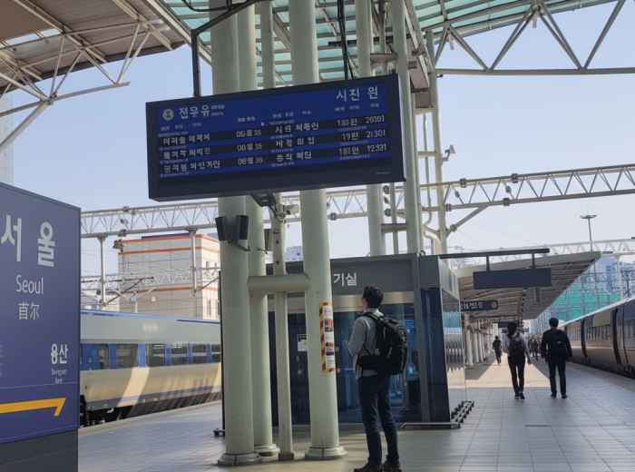 Solo traveler checking departure board at a quiet morning platform, backpack ready