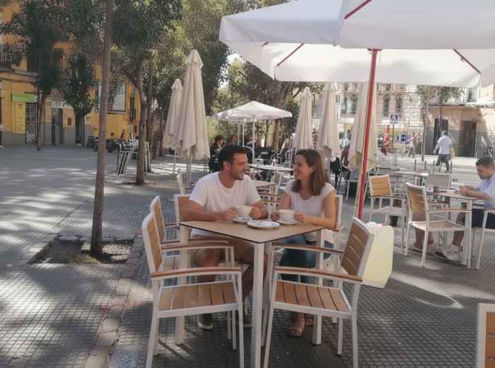 Quiet neighborhood street with locals chatting at café tables in the morning