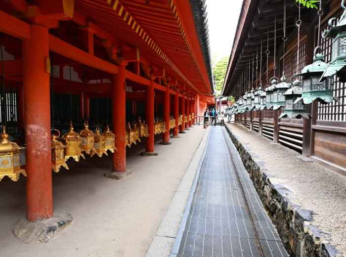 Lantern-lined walkway at Kasuga Taisha Shrine with red columns and hanging bronze lanterns