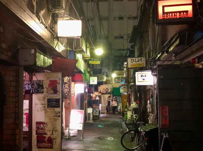 Narrow alley in Golden Gai at night with small bar entrances and illuminated signs