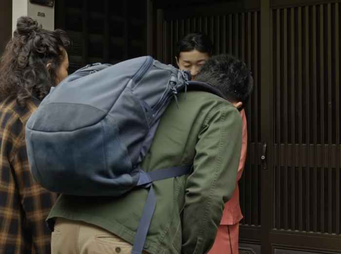 Travelers bowing politely while greeting a local at the entrance of a Japanese home