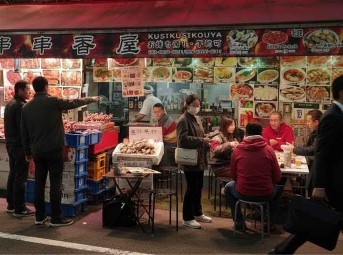 Street food stall with people ordering and eating at night, Tokyo