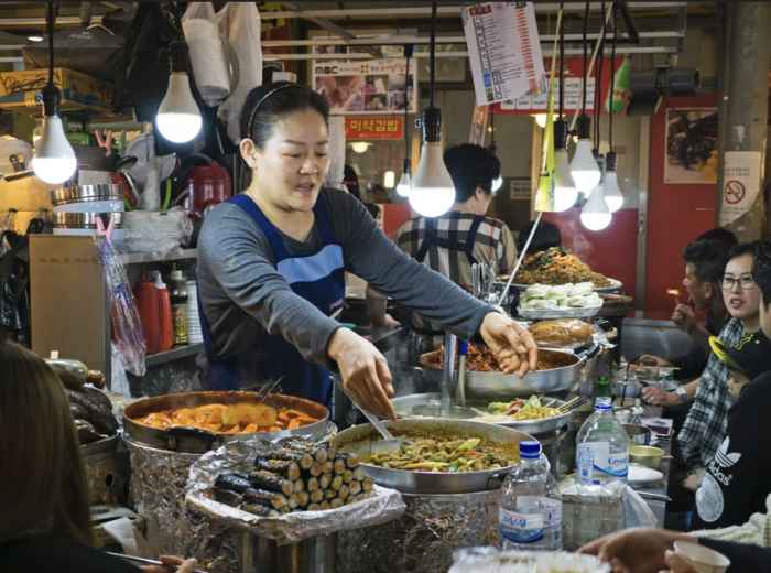 Street food vendor serving hot dishes under bare bulbs at a Seoul market