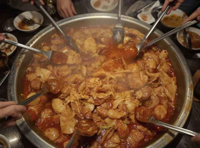 Spicy dakgalbi cooking in a communal pan with chicken, cabbage, and rice cakes