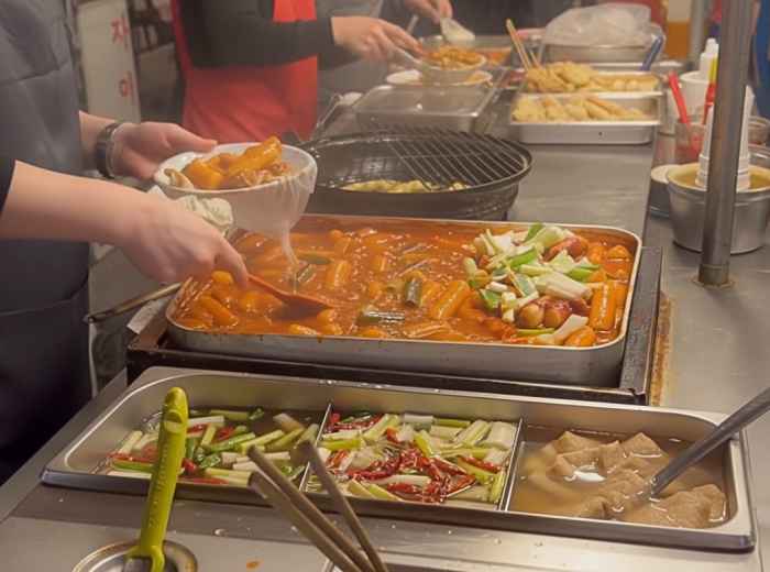 Bright red tteokbokki bubbling in a wide pan at a street food stall