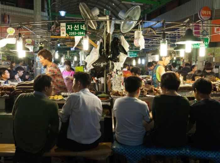 Busy food stall at Gwangjang Market with shared bench seating