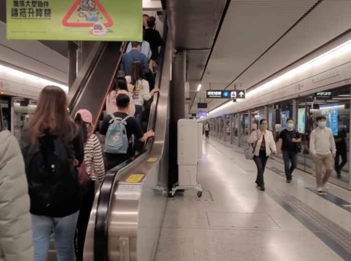 Commuters ride an escalator and walk along a Hong Kong MTR station platform