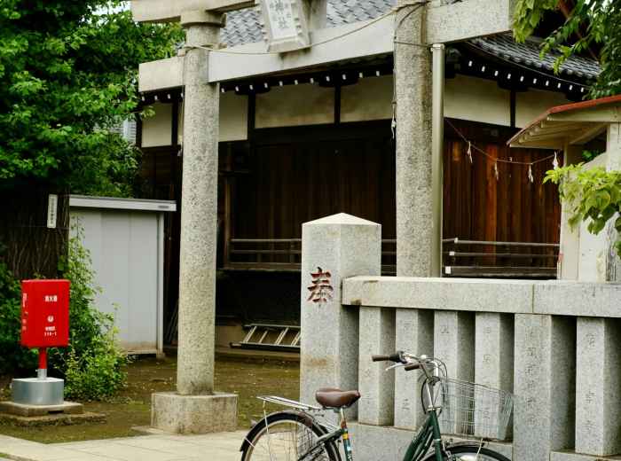 A small neighborhood shrine squeezed between modern buildings with offerings at its entrance