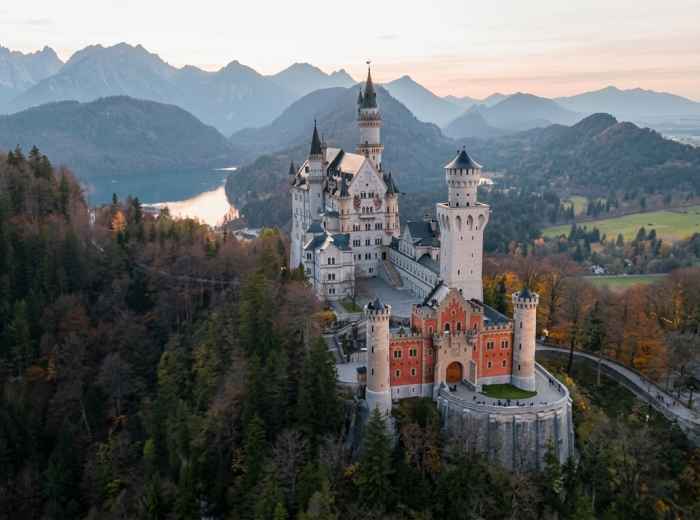 Neuschwanstein Castle rises above forests with the Bavarian Alps beyond 