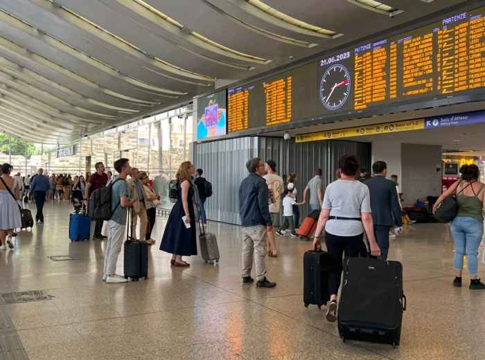 Travelers beneath departure boards at Roma Termini station 