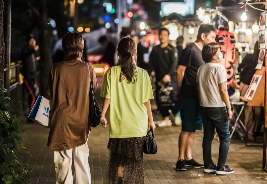 two woman walking down a busy steet during the evening